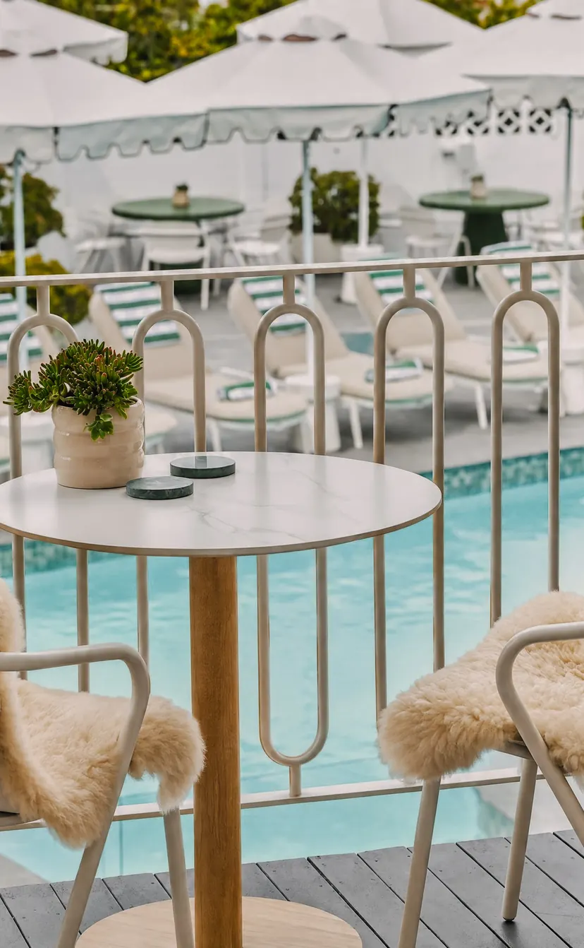 A suite balcony: two chairs with sheepskins and a table, the pool and the umbrellas below